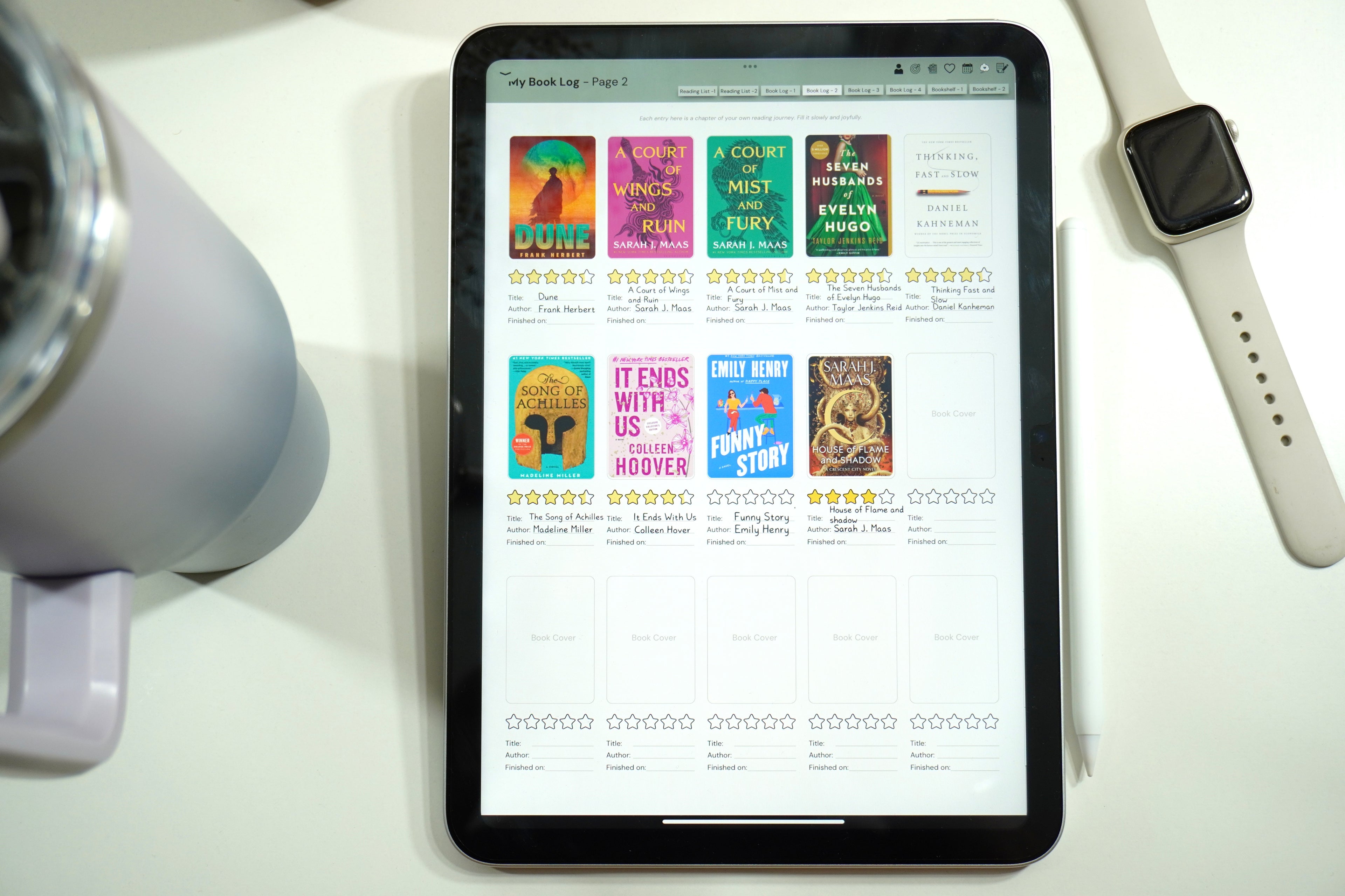 Book log page of the digital reading journal open in an iPad in the Goodnotes app, placed on a study table with an iwatch and stanley mug on the side. 